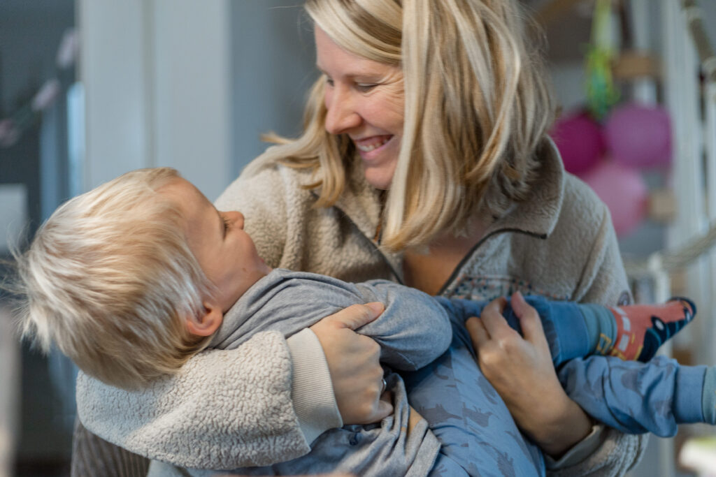 Mama hält Kind im Arm, beide lachen sich an