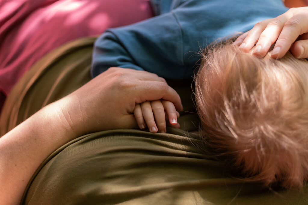 Ein Kind liegt auf der Brust seiner Mutter. Sie hält seine Hand und streichelt ihm über den Kopf.