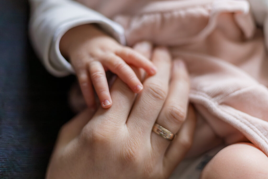 Eine Babyhand liegt auf einer Hand eines Erwachsenen.