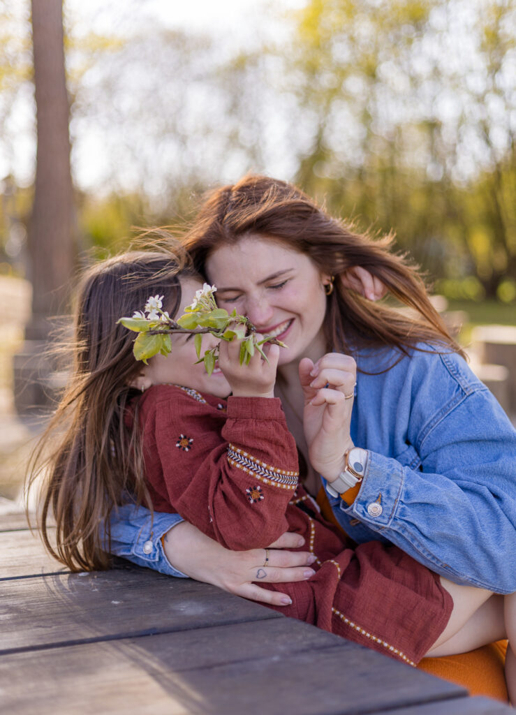 Eine Frau sitzt an einem Tisch, auf ihrem Schoß sitzt ein Kind und hält eine Blume in der Hand. Beide lachen.